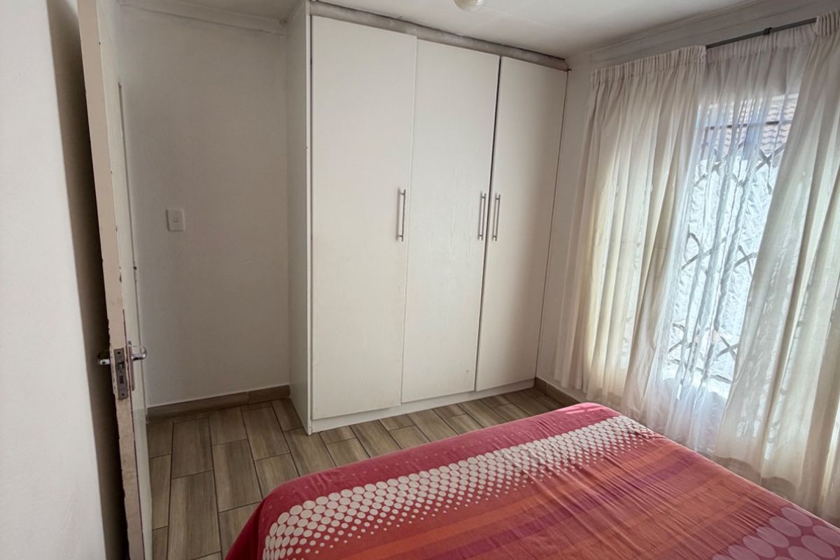 A functional bedroom featuring tiled flooring, a built-in wardrobe, and a window fitted with a security gate.