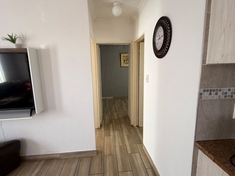 A clean, neutral hallway featuring modern wood-look floor tiles, coved cornicing, and a ceiling access hatch, providing access to adjacent rooms.