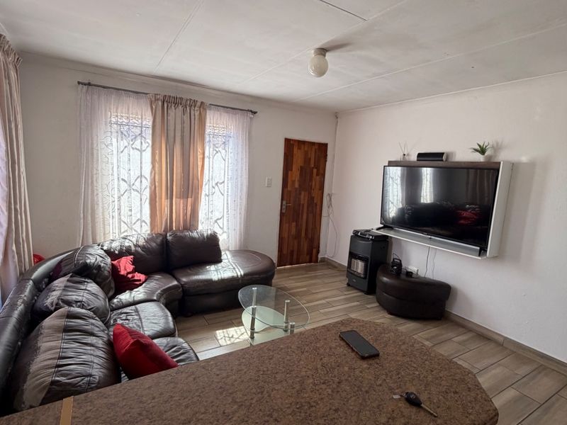 Open plan living area featuring tiled flooring, a built-in kitchen counter, and security bars on the windows.