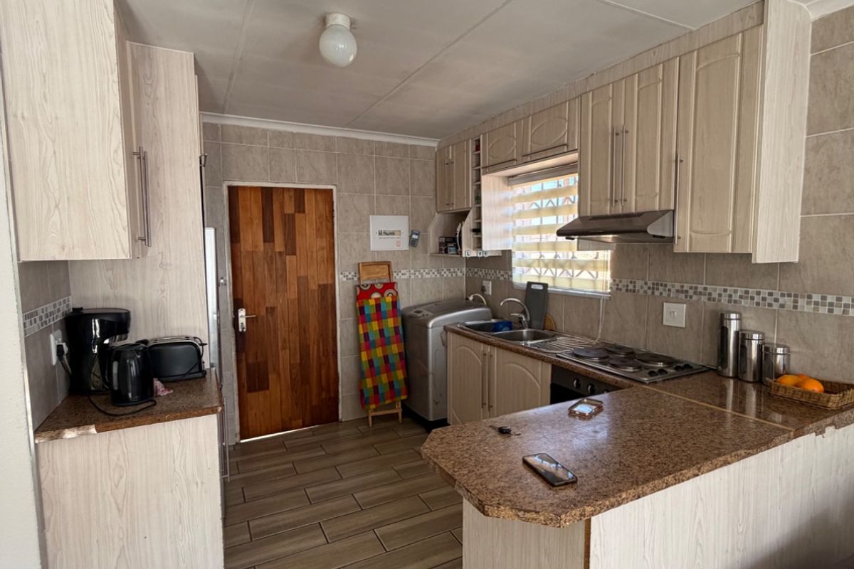 A functional kitchen featuring light wood-look cabinetry, granite countertops, a built-in hob with extractor fan, and tiled flooring throughout.
