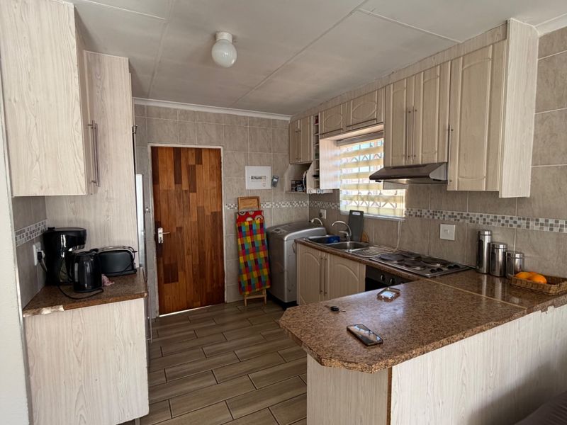 A functional kitchen featuring light wood-look cabinetry, granite countertops, a built-in hob with extractor fan, and tiled flooring throughout.