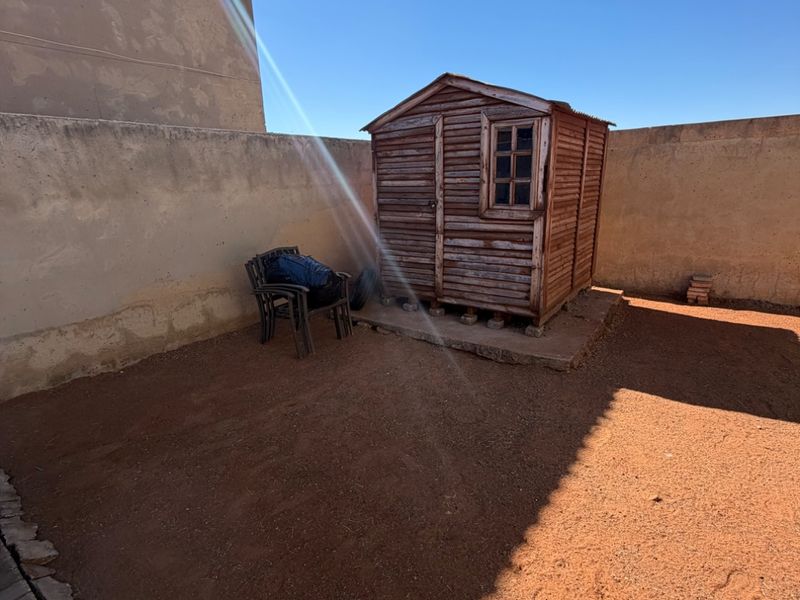 Rear garden area featuring a weathered wooden storage shed and perimeter boundary walls, offering potential for landscaping or outdoor improvement.