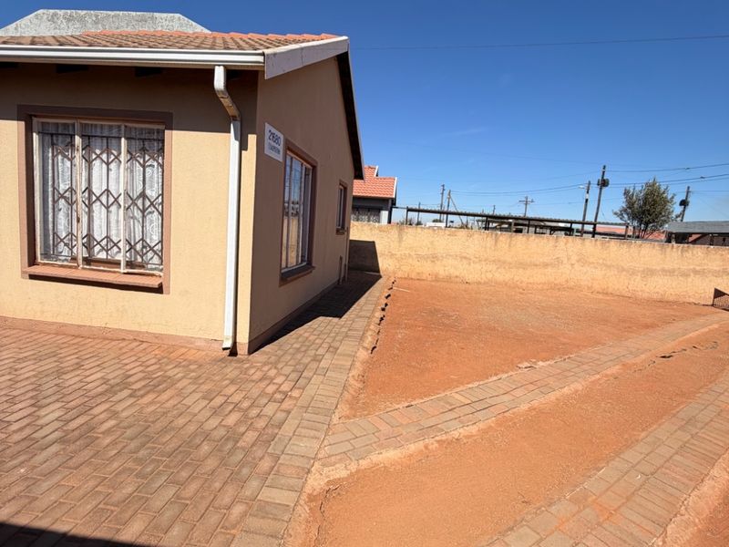 Rear exterior view of the house featuring brick paving, a perimeter wall, and security bars on the windows.