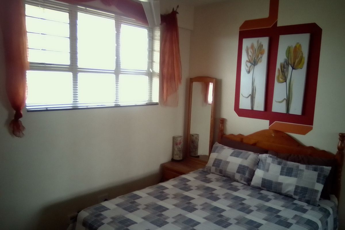 A bedroom featuring a ceiling fan and a large window with aluminium frames, providing natural light to the space.