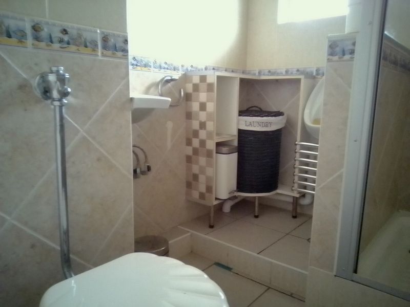 A compact bathroom featuring tiled finishes, a wall-mounted urinal, and built-in shelving. The space requires cosmetic updates to improve its overall condition.