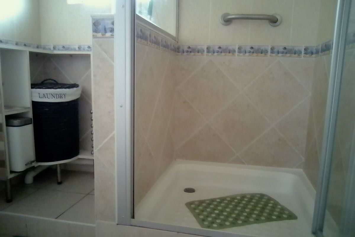 A functional bathroom featuring a shower enclosure with tiled walls and a grab rail, alongside a dedicated utility area for laundry.