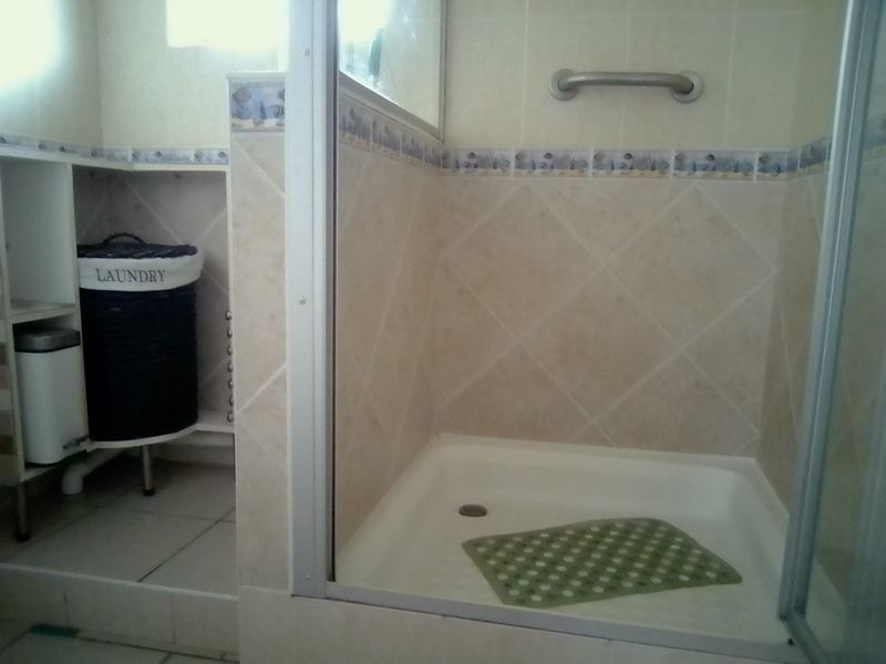 A functional bathroom featuring a shower enclosure with tiled walls and a grab rail, alongside a dedicated utility area for laundry.