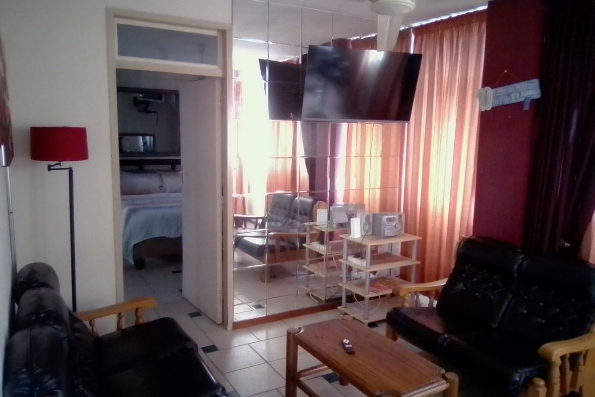 Living room featuring tiled flooring, a ceiling fan, and a large mirrored wall, with an adjacent view into a bedroom.