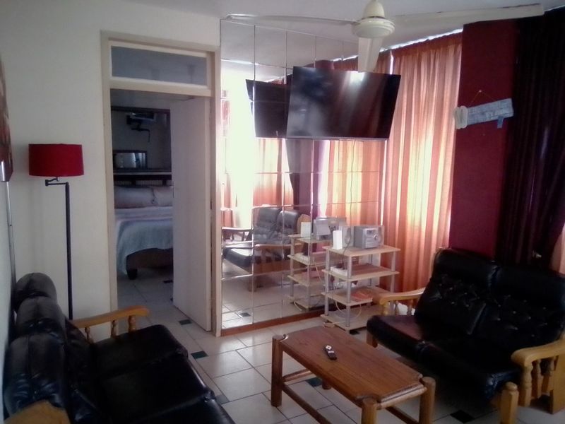 Living room featuring tiled flooring, a ceiling fan, and a large mirrored wall, with an adjacent view into a bedroom.