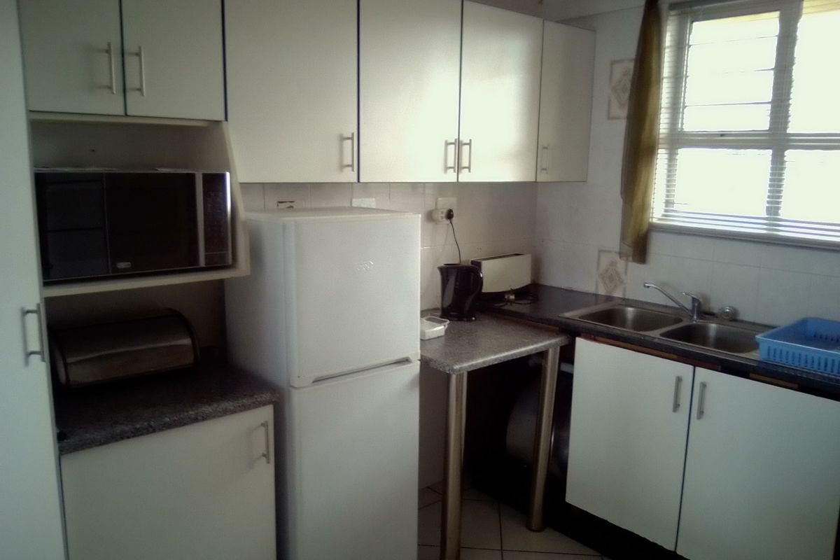 A functional kitchen featuring white cabinetry, laminate countertops, a double stainless steel sink, and tiled flooring, offering a practical layout for daily use.
