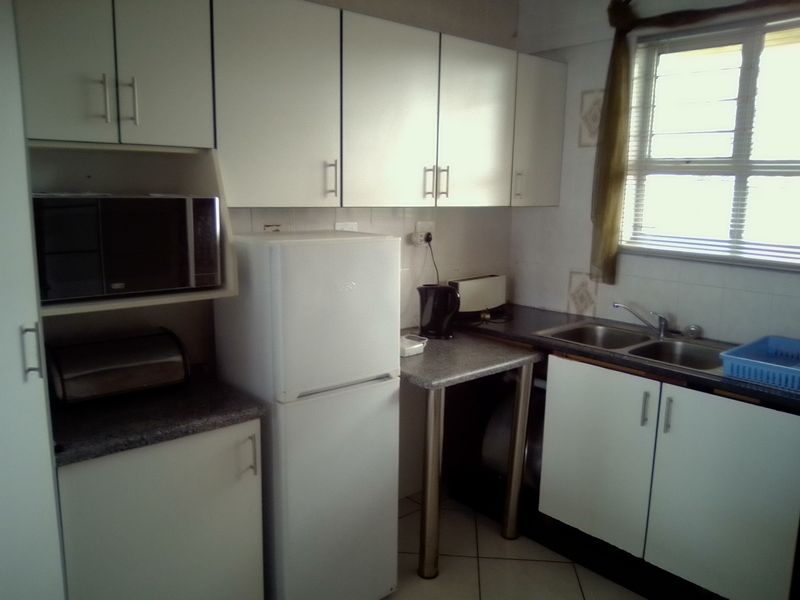 A functional kitchen featuring white cabinetry, laminate countertops, a double stainless steel sink, and tiled flooring, offering a practical layout for daily use.