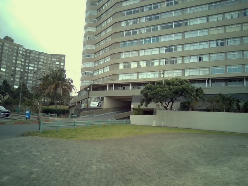 Exterior view of a multi-story apartment building featuring a paved driveway, concrete facade, and surrounding landscaped grounds.