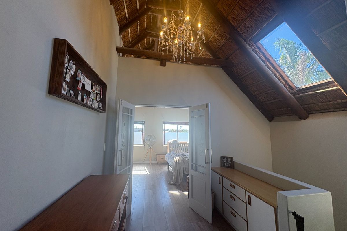 A spacious bedroom featuring a high exposed thatch ceiling, a large skylight, and double doors leading to an adjoining room with timber flooring.