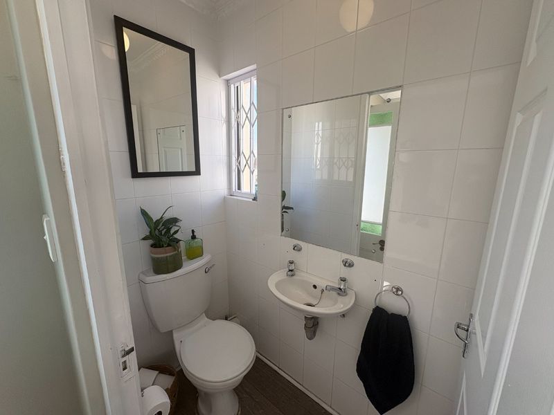 A compact guest bathroom featuring white wall tiles, a wall-mounted basin, and a toilet with a security-gated window.