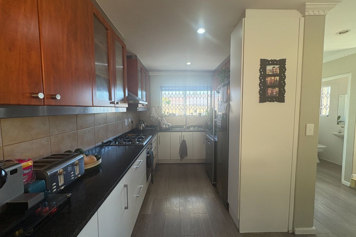 A functional galley-style kitchen featuring wood-tone upper cabinets, white lower cabinetry, dark granite countertops, and a gas hob with an extractor fan.