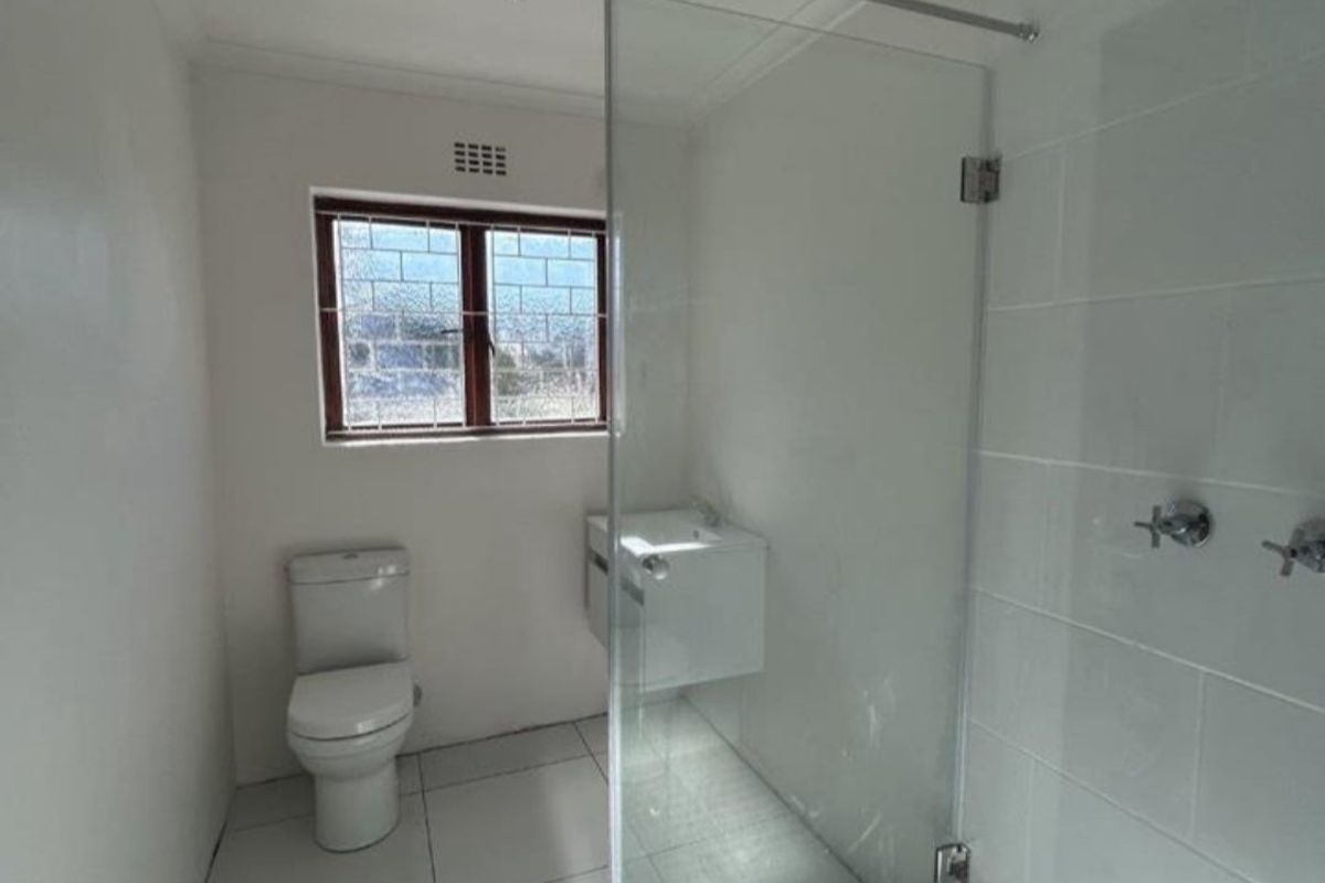 Modern bathroom featuring a glass-enclosed walk-in shower, wall-mounted vanity, and clean white tiled finishes throughout.
