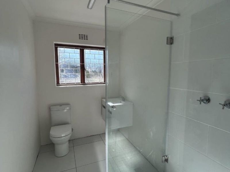 Modern bathroom featuring a glass-enclosed walk-in shower, wall-mounted vanity, and clean white tiled finishes throughout.