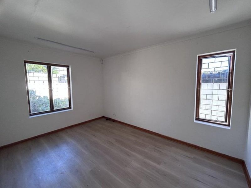 A bright, empty bedroom featuring light-toned laminate flooring, neutral walls, and windows fitted with security burglar bars.