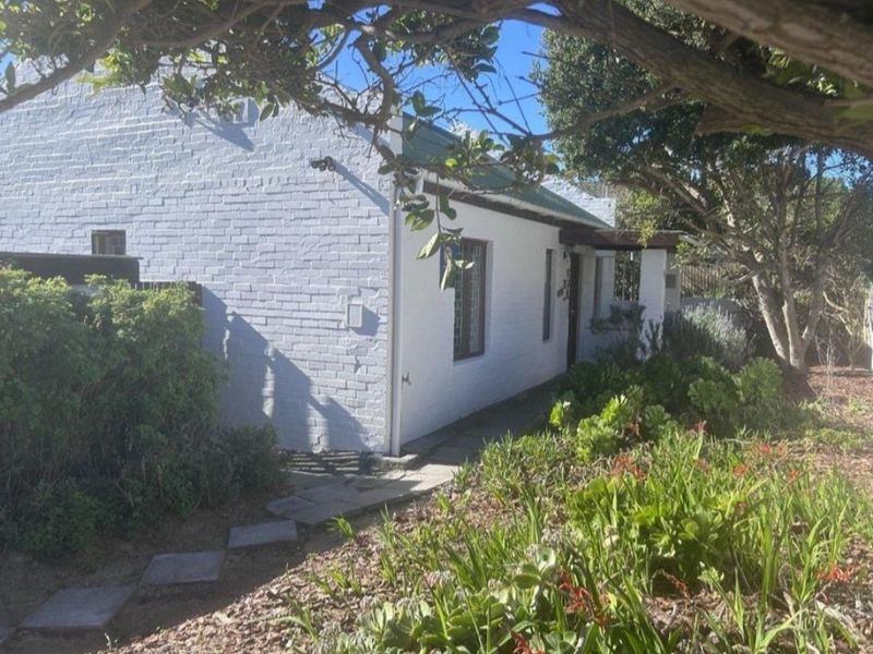 A charming cottage-style home featuring a painted brick exterior, a stone pathway, and a well-established garden.
