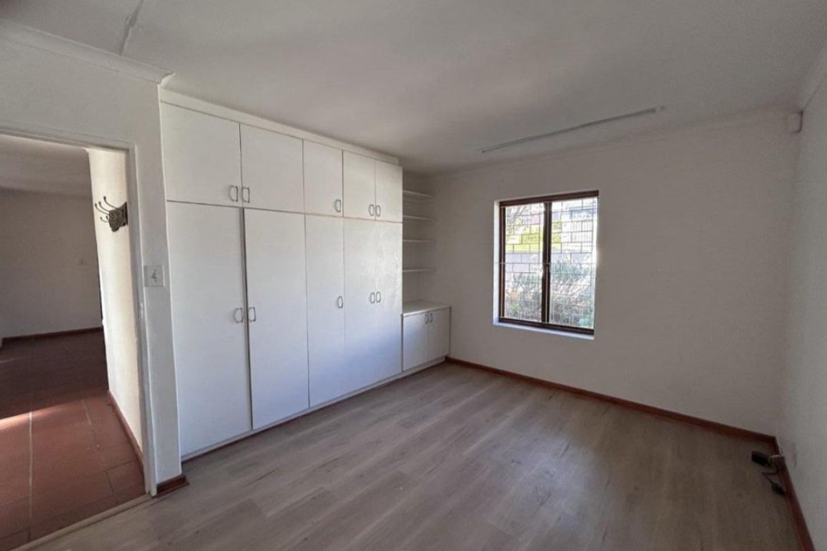A bright, empty bedroom featuring built-in cupboards, laminate flooring, and security bars on the window, offering a clean canvas for personalization.