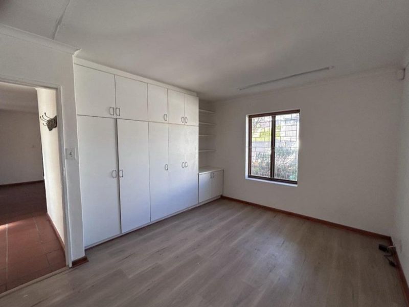 A bright, empty bedroom featuring built-in cupboards, laminate flooring, and security bars on the window, offering a clean canvas for personalization.