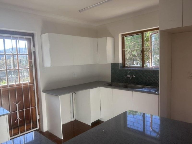 A functional kitchen featuring white cabinetry, grey countertops, a stainless steel sink, and a tiled backsplash, with direct access to the exterior.
