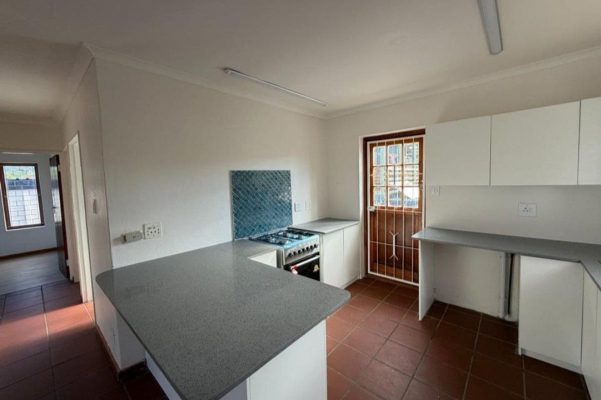 A functional kitchen featuring white cabinetry, grey countertops, a freestanding stove, and terracotta-style floor tiles with direct access to the exterior.