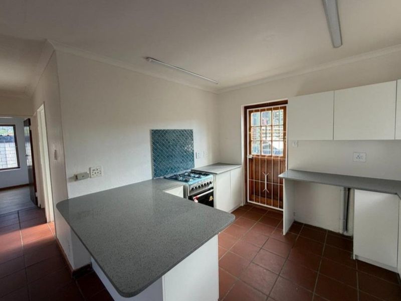 A functional kitchen featuring white cabinetry, grey countertops, a freestanding stove, and terracotta-style floor tiles with direct access to the exterior.