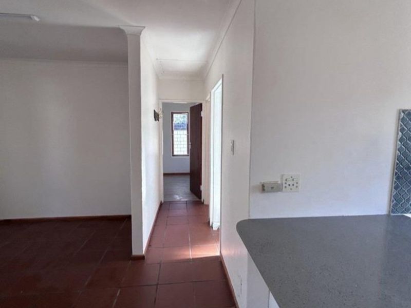 A bright, empty hallway featuring tiled flooring and a stone countertop, leading towards a doorway with a window view.