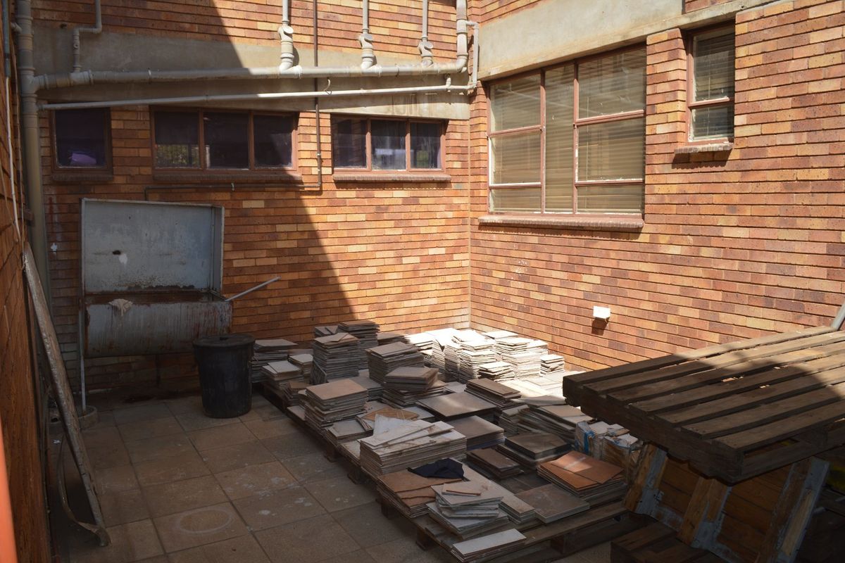 A rear exterior utility area featuring exposed brick walls, external plumbing, and a metal utility sink, currently used for storage.