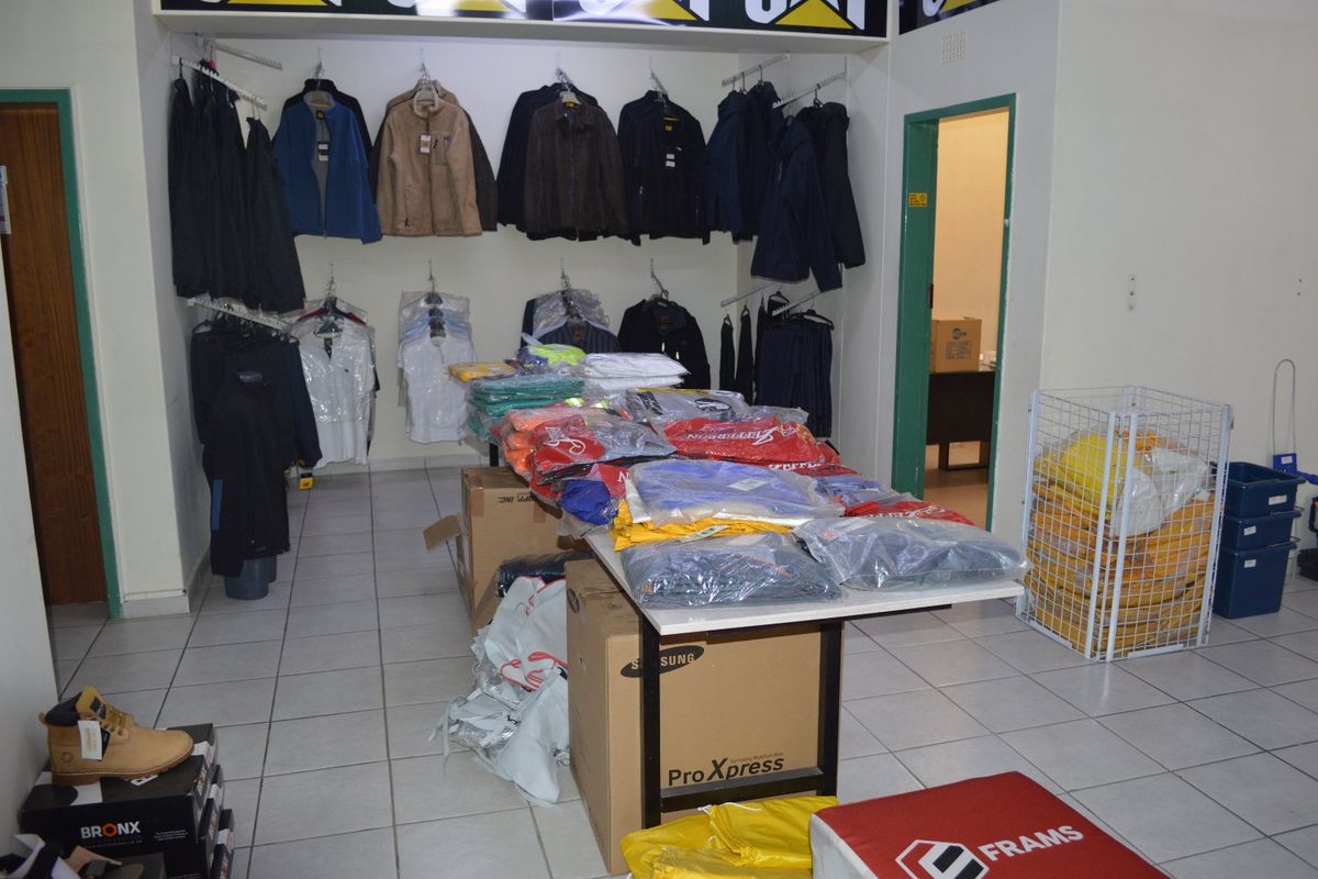 A commercial retail space featuring tiled flooring, wall-mounted clothing display rails, and a secondary doorway leading to a back office area.