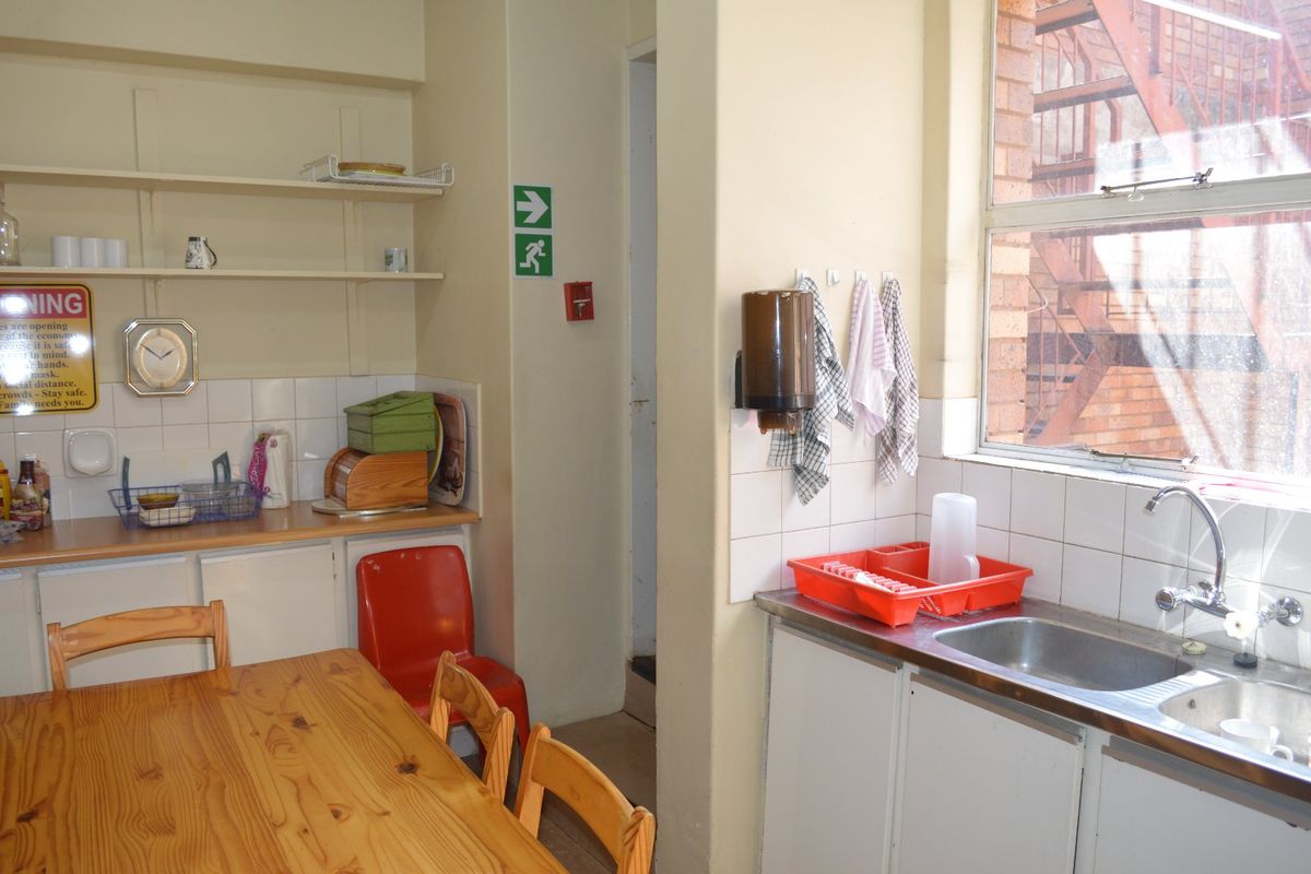 A functional commercial kitchen area featuring a stainless steel sink, tiled splashbacks, and built-in cabinetry with open shelving for storage.