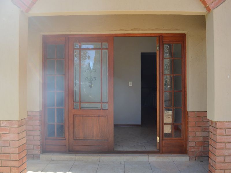 A covered entrance featuring a wooden sliding door with glass panels, set against a brick and plaster facade with tiled flooring.