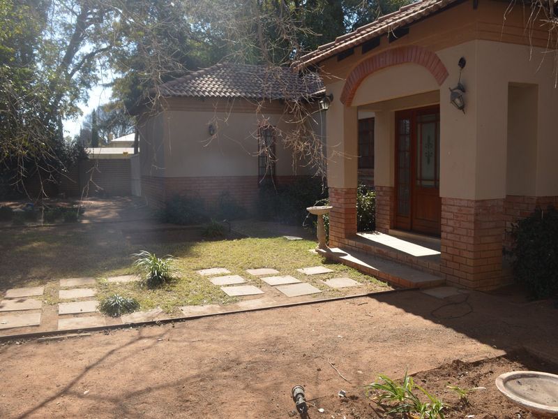 Front view of a single-story house featuring a covered entrance porch, brick facade, and a garden area with paved pathways.