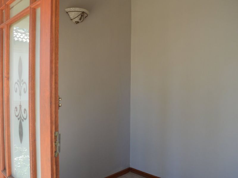 A clean, neutral-toned entryway featuring a decorative timber-framed glass door and a wall-mounted light fixture.