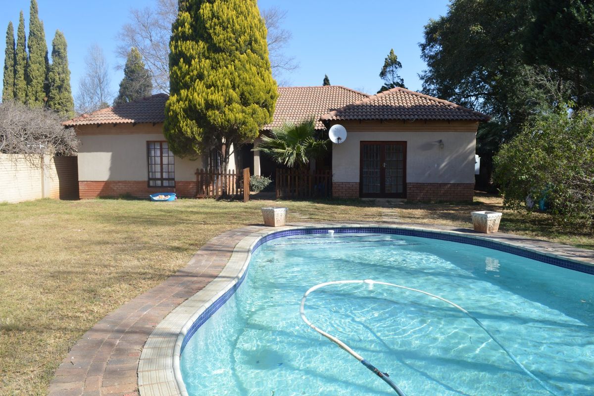 Rear view of the property featuring a swimming pool, paved surround, and a tiled roof house with french doors opening to the garden.
