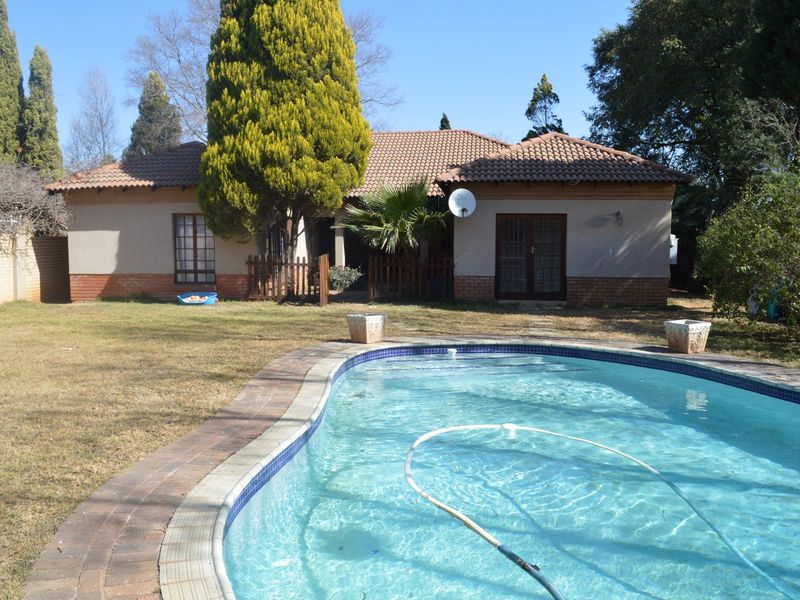 Rear view of the property featuring a swimming pool, paved surround, and a tiled roof house with french doors opening to the garden.