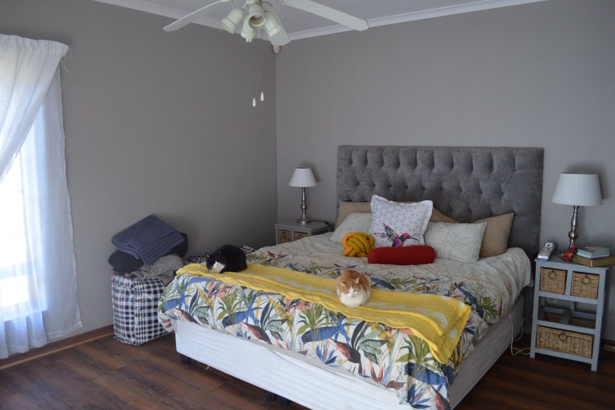 A well-maintained bedroom featuring laminate flooring, neutral grey walls, and a ceiling fan.