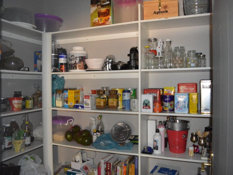 A functional walk-in pantry or scullery area featuring extensive built-in white shelving for organized storage.