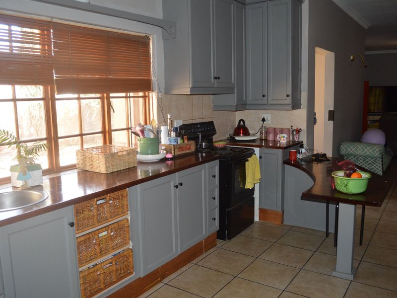 A functional kitchen featuring grey cabinetry, wooden countertops, a stainless steel sink, and tiled flooring, with a breakfast nook area.