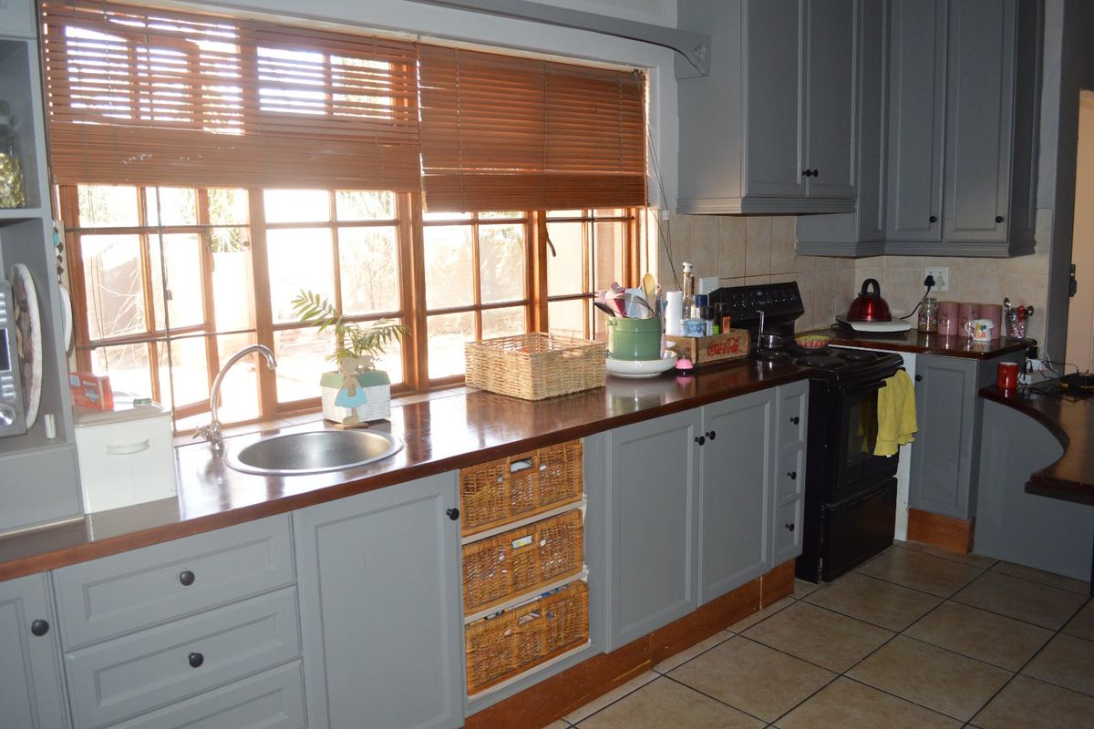 A functional kitchen featuring grey cabinetry, wooden countertops, a stainless steel sink, and tiled flooring with natural light from large timber-framed windows.