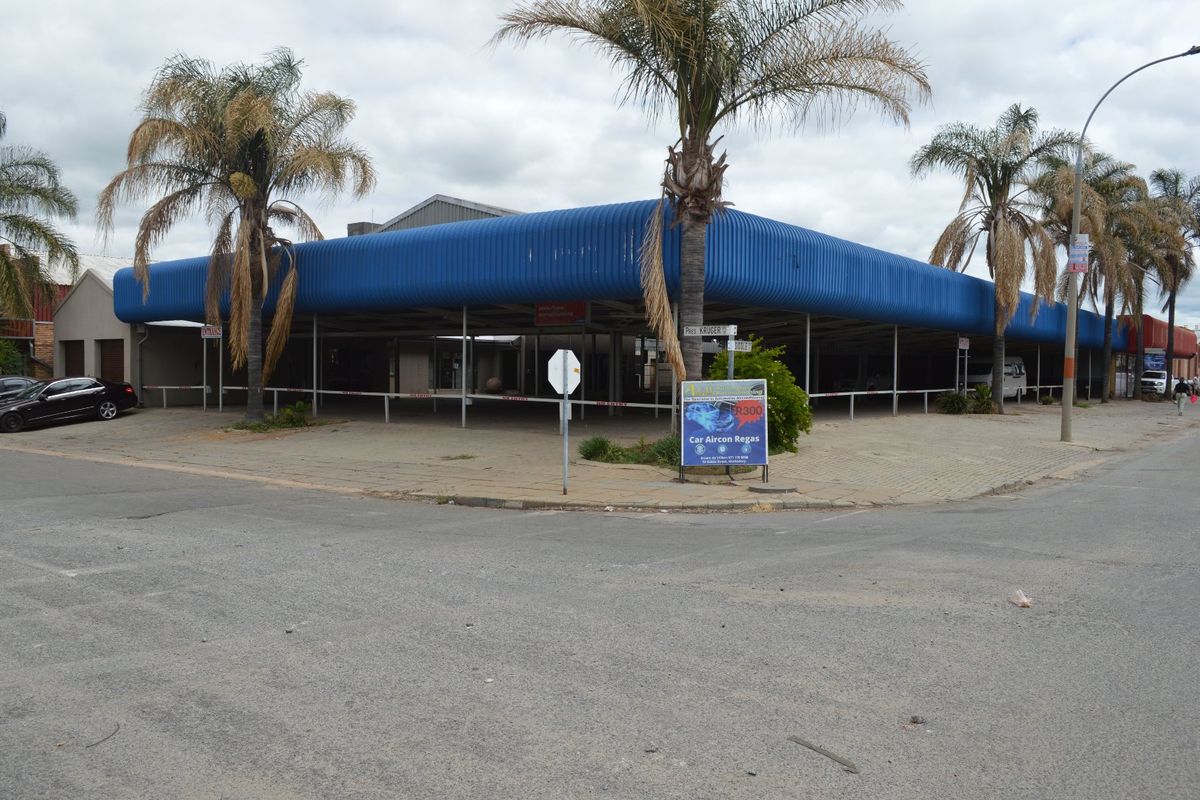 Corner commercial property featuring a large open-plan forecourt area with a prominent blue corrugated metal roof structure and paved exterior.
