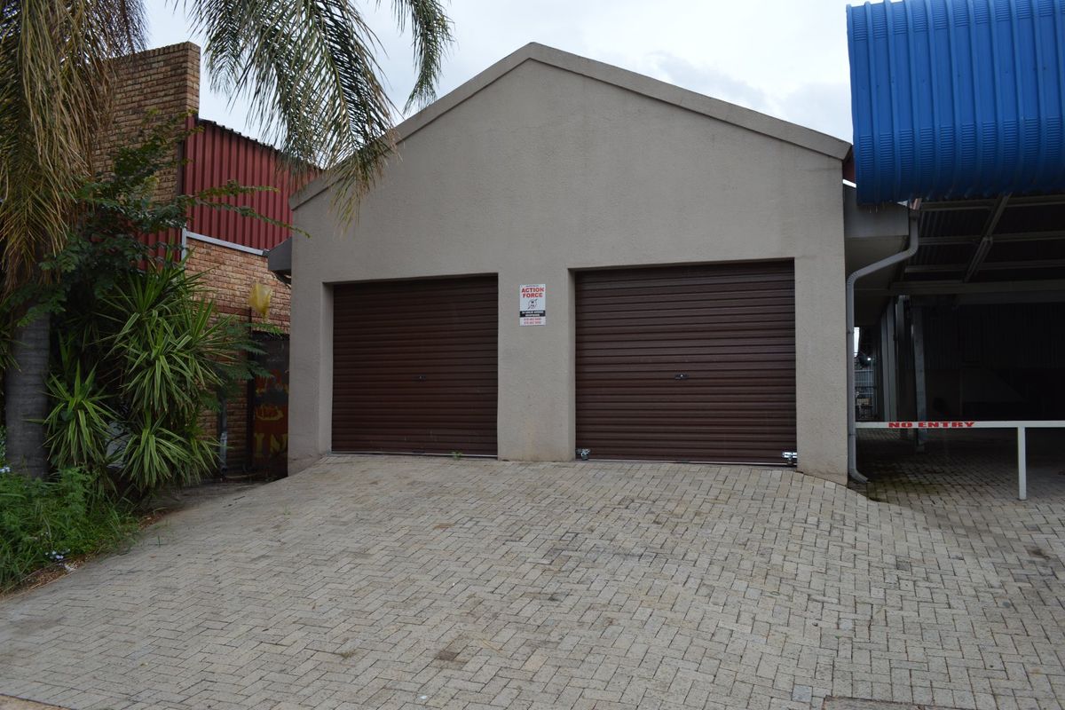 A commercial property featuring a double garage with brown roller doors and a paved driveway entrance.