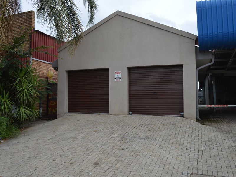 A commercial property featuring a double garage with brown roller doors and a paved driveway entrance.