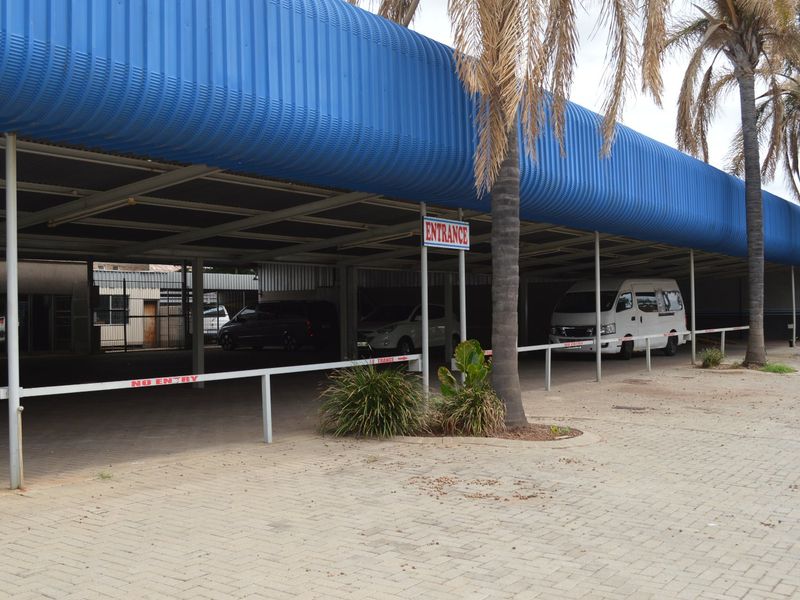 Commercial property exterior featuring a large blue corrugated metal roof canopy providing covered parking and a paved driveway entrance.