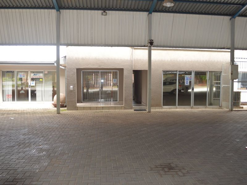 Commercial property frontage featuring a large covered parking area with paved driveway and multiple glass entrance doors.
