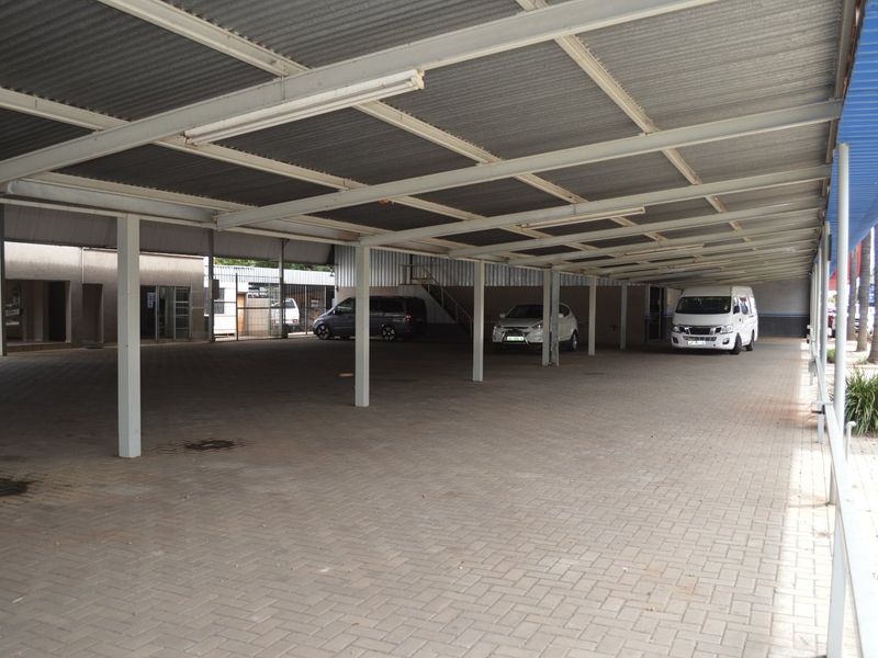 A large, covered commercial parking area featuring a corrugated metal roof supported by steel columns and paved ground surface.