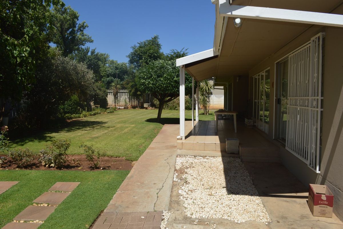 A rear view of the property featuring a covered patio with tiled flooring, sliding glass doors with security gates, and a well-maintained garden.