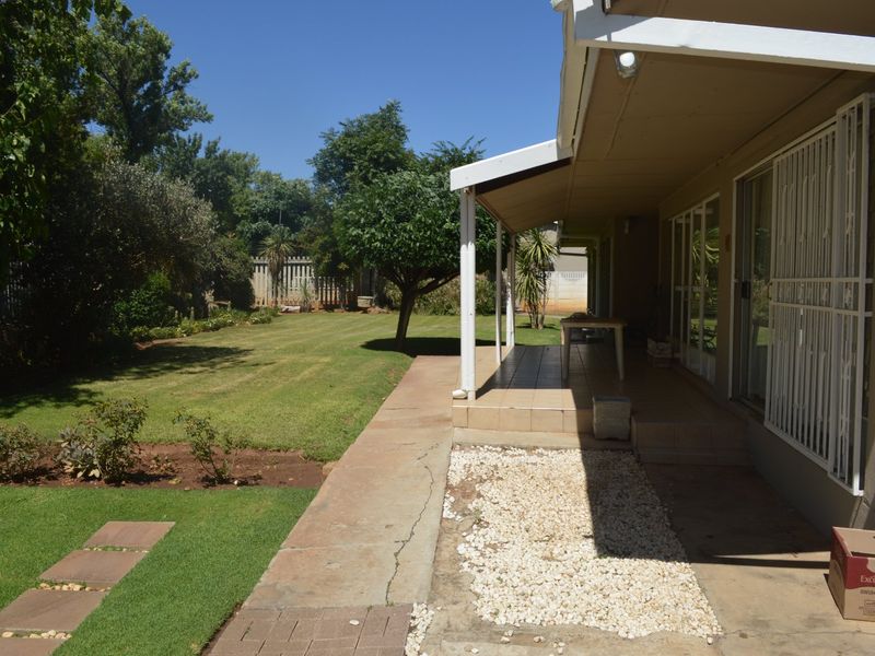 A rear view of the property featuring a covered patio with tiled flooring, sliding glass doors with security gates, and a well-maintained garden.