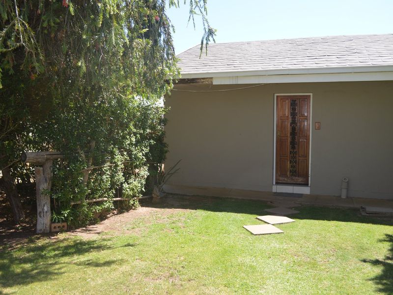 Rear exterior view of the commercial property featuring a lawn area, paved walkway, and a timber entrance door with visible roof fascia damage.